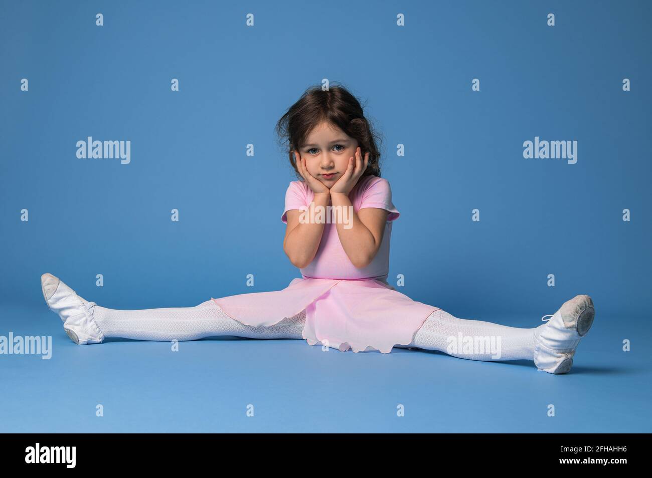 Cute ballerina in pink dress perfecting twine while sitting on blue background with copy space Stock Photo