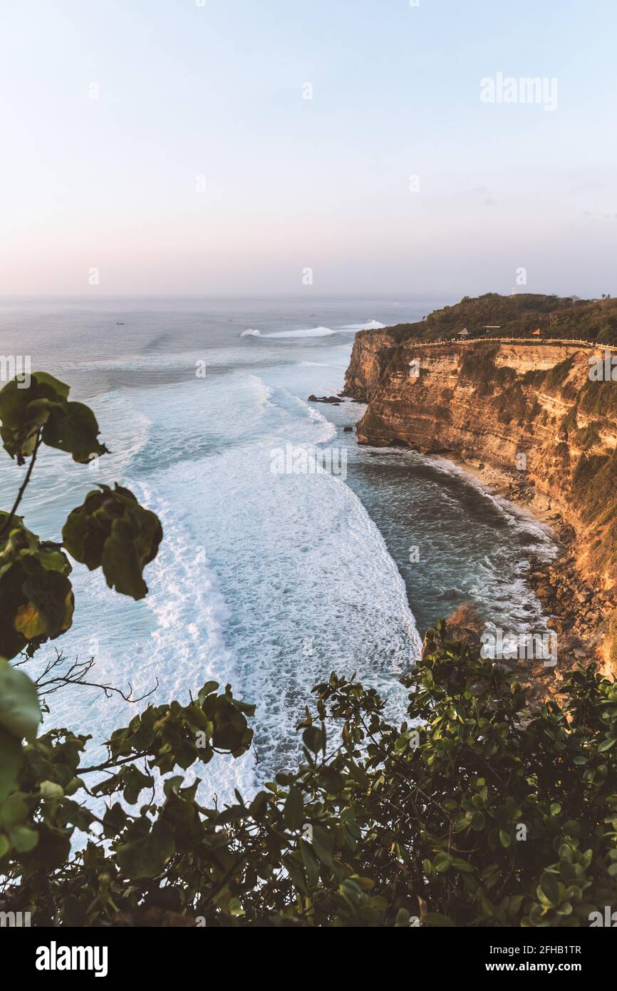 Swashed Cliff Rough rocky cliff washed by wavy foamy sea under cloudless blue sky in ...