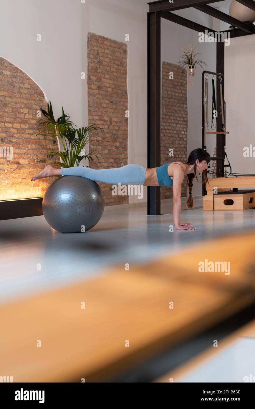 Side view of fit female in sportswear doing exercise on fit ball during ...