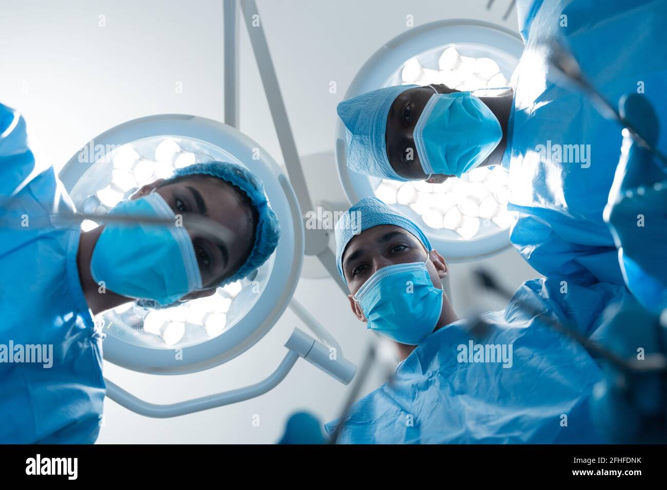Diverse surgeons wearing face masks and protective clothing in operating theatre Stock Photo