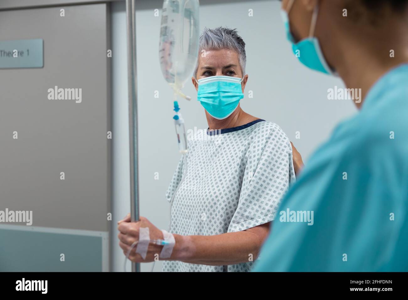 Caucasian female patient wearing face mask standing on corridor with ...