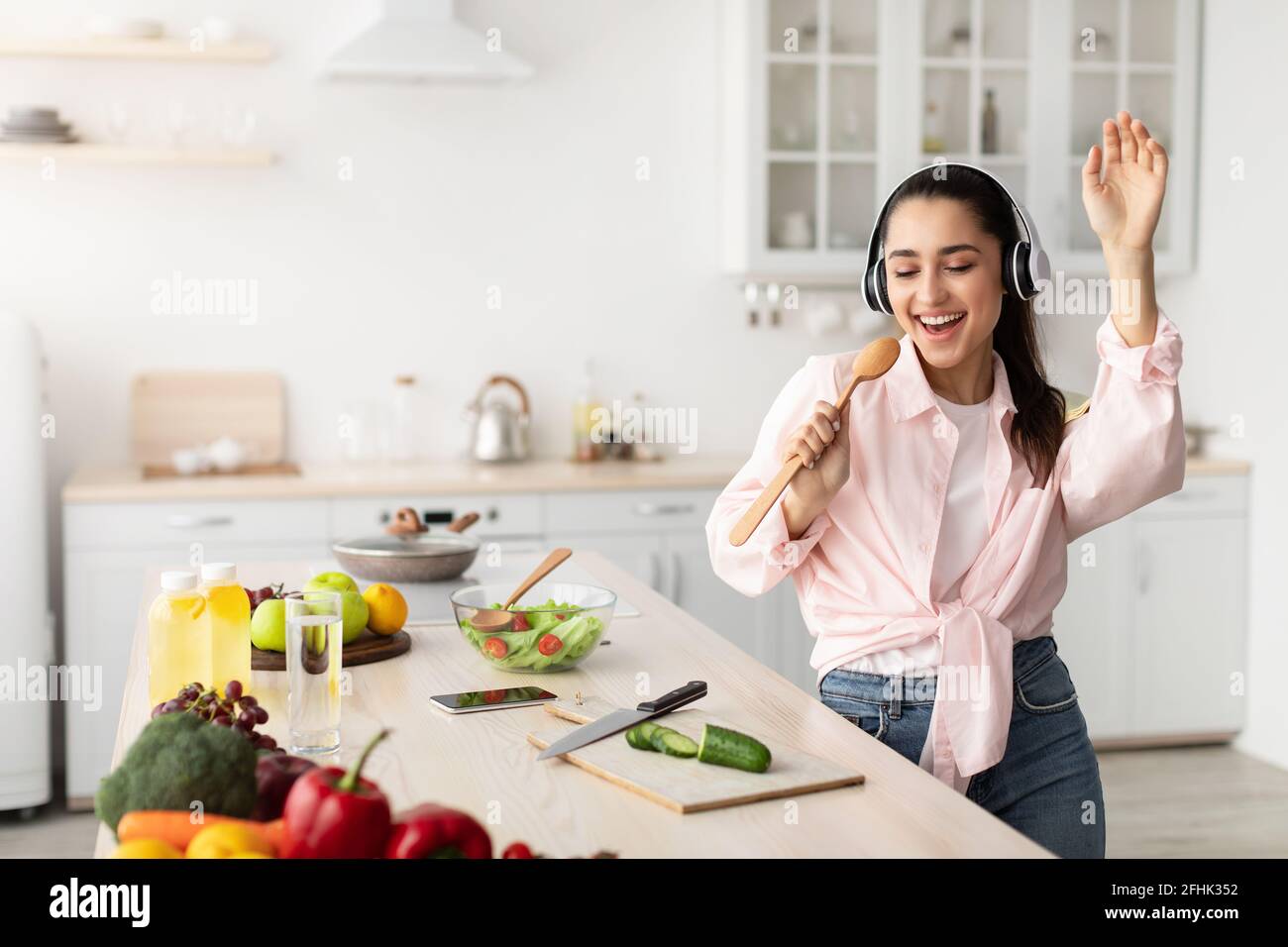 Portrait of smiling young woman singing and dancing in kitchen Stock Photo