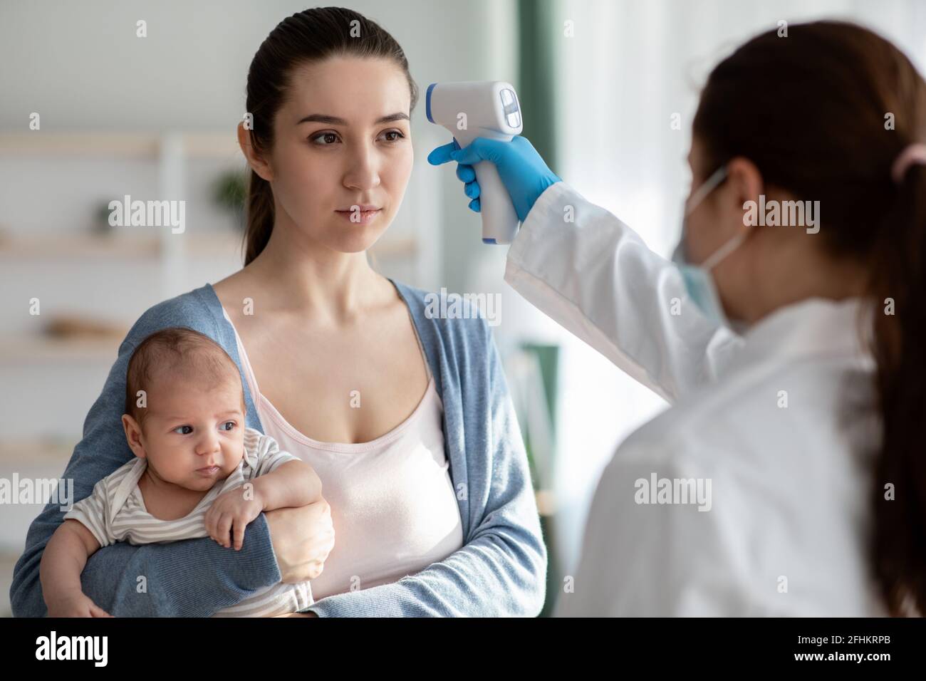 Doctor Checking Temperature For Young Woman And Newborn Baby With Infrared Thermometer Stock Photo