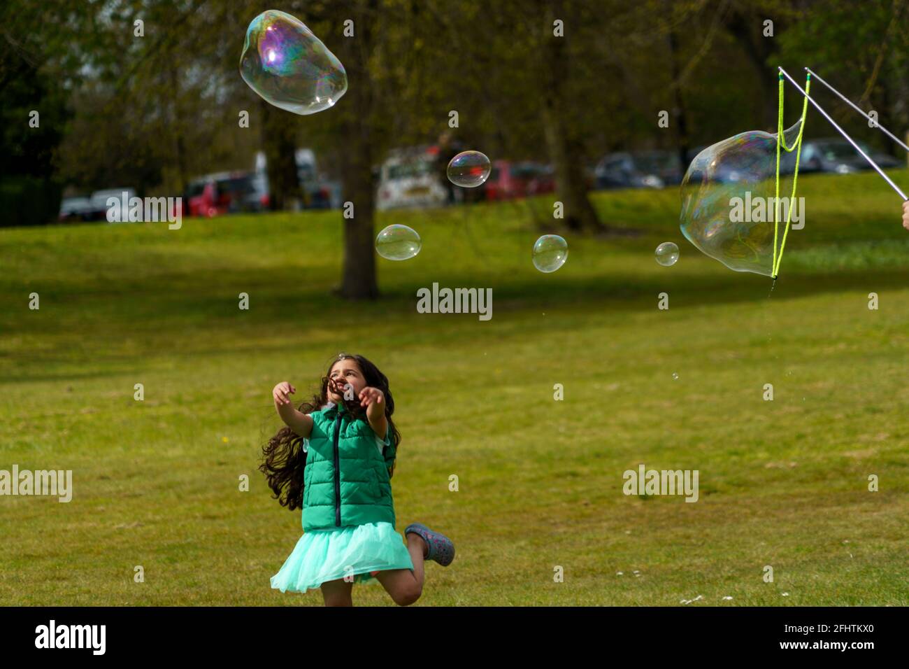 Harrogate park where a young girl is chasing the soapy bubbles created with a Bubble Wand, North Yorkshire, England, UK. Stock Photo