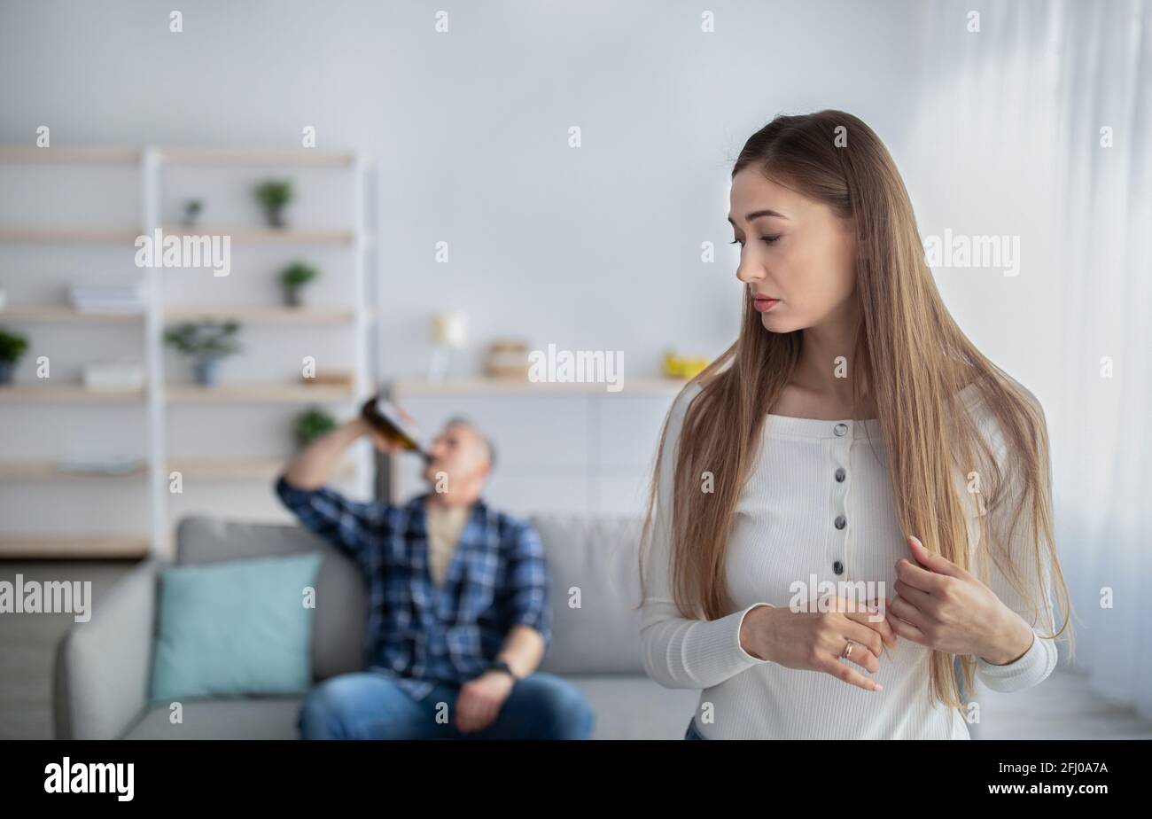 Alcohol addiction and family problems. Sad middle-aged woman looking over her shoulder at her drunk husband Stock Photo