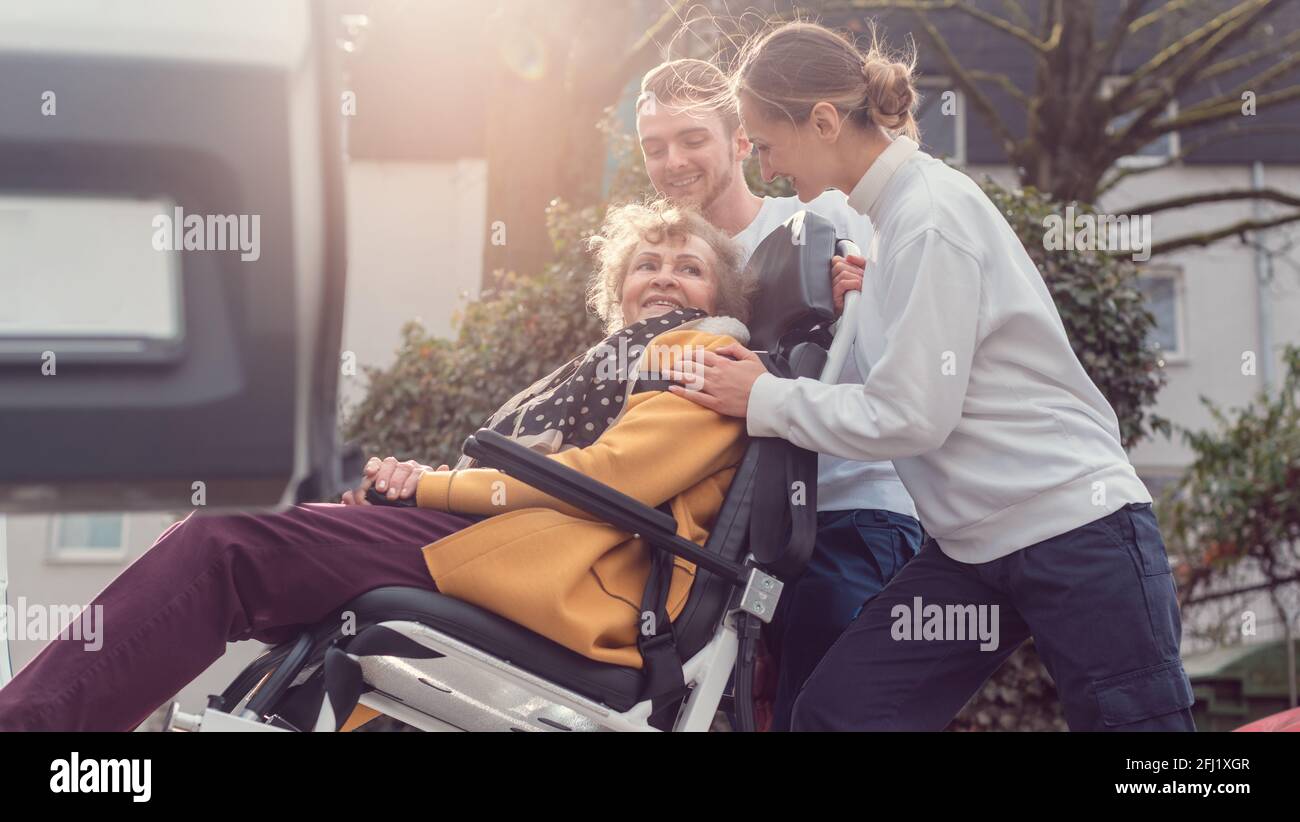 Two helpers picking up disabled senior woman for transport Stock Photo