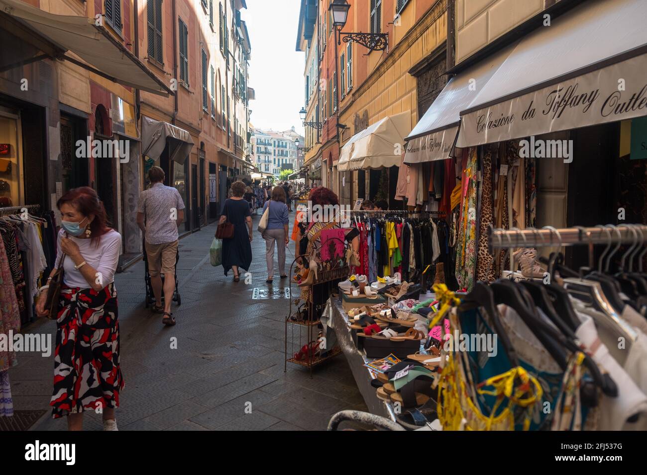 Clothes are for sale outside a store in a narrow shopping street in the pedestrian area of the old town of Rapallo. Stock Photo