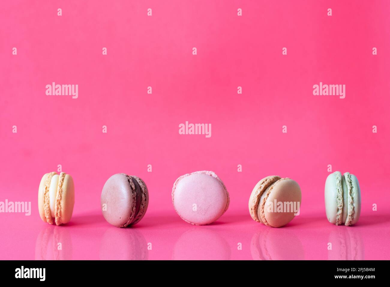 Close Up Fresh Colorful Macaroons In A Row Isolated On Pink Background, Sweet Colorful Biscuits Heap Lined Up With Reflection On Table Stock Photo