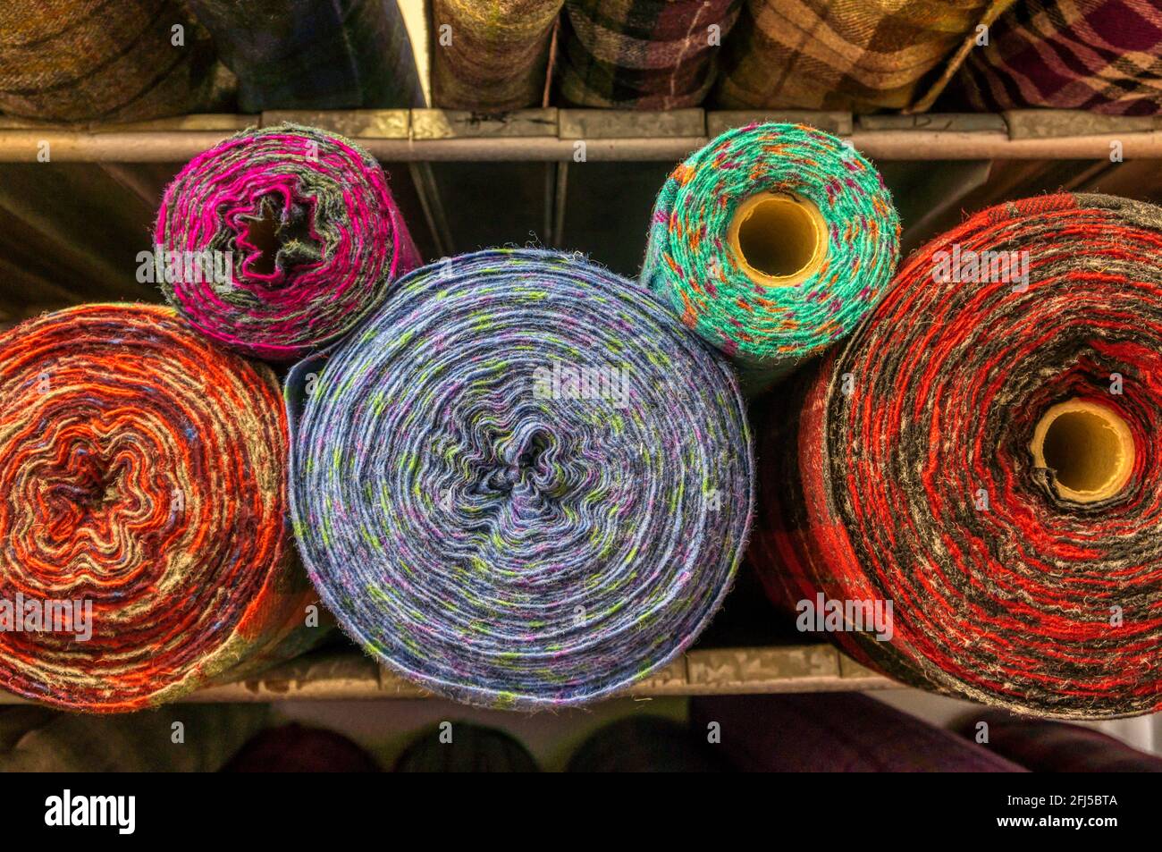 Colourful rolls of dyed Harris tweed on warehouse shelves. Stock Photo