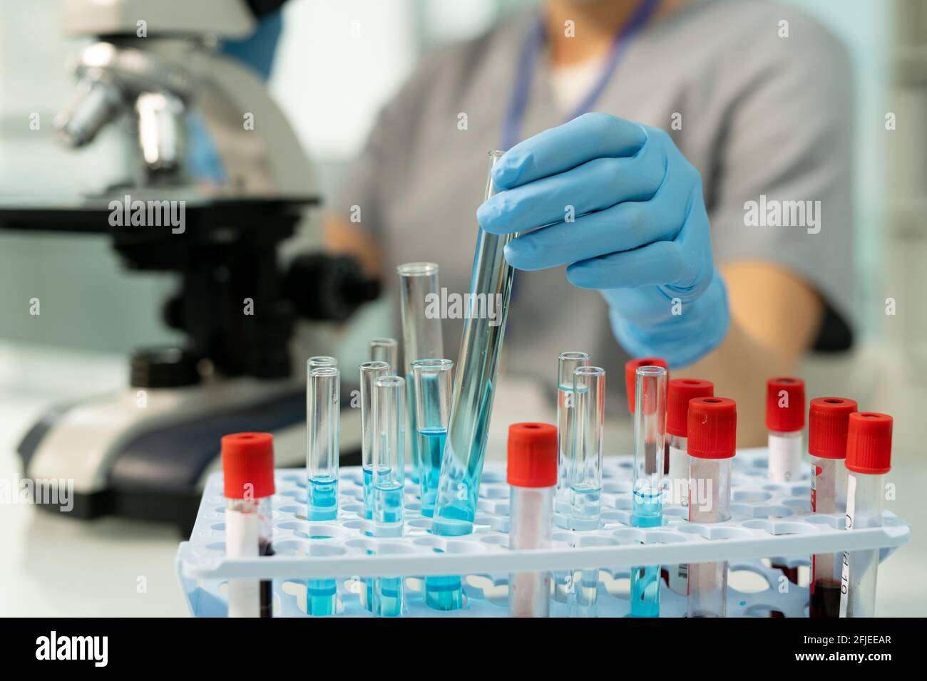 Close-up of unrecognizable medical researcher in gloves putting test tube of blue liquid into rack with blood samples Stock Photo