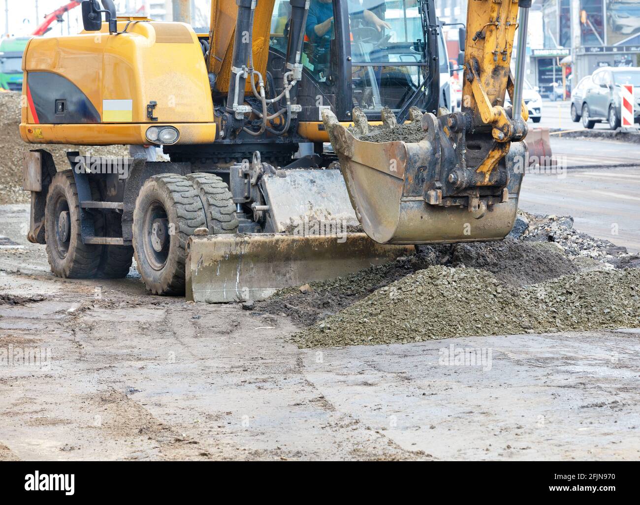 A road excavator bucket evenly distributes rubble to create a foundation on a dirt construction site throughout the working day. Copy space. Stock Photo