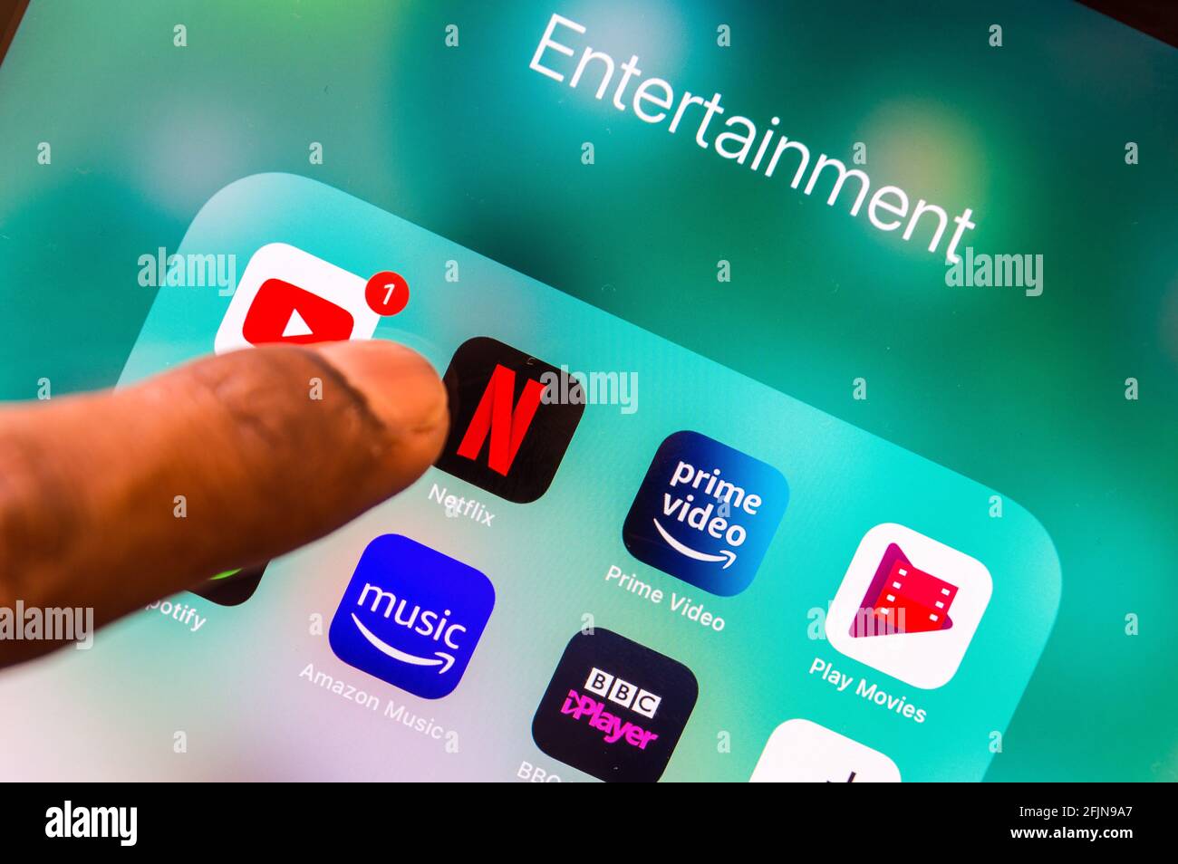 Adult male finger opening Netflix app from an Entertainment folder on personal digital device Stock Photo