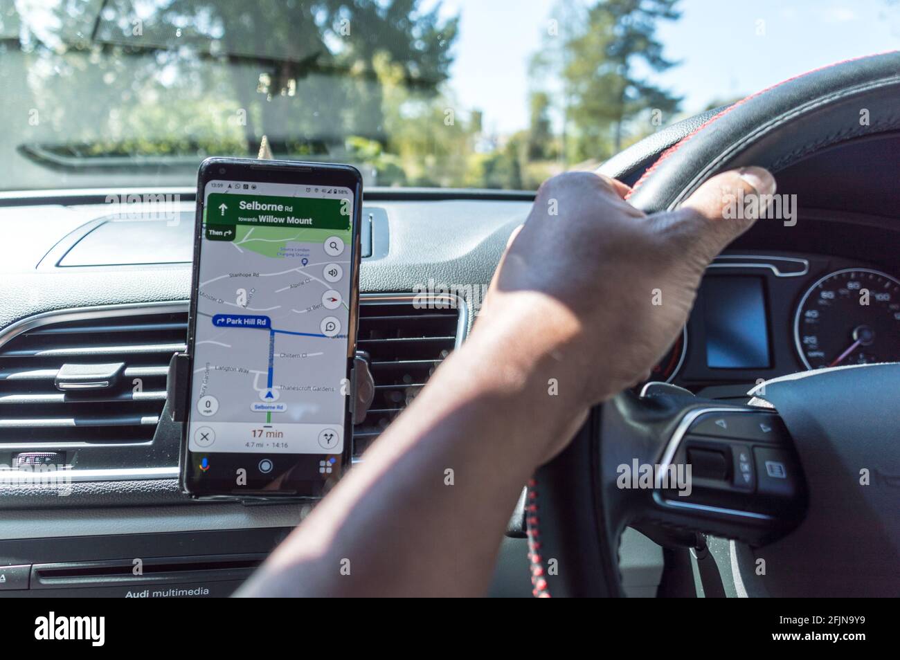 Google maps app GPS on smarphone in car with view of steering wheel and hands of driver Stock Photo