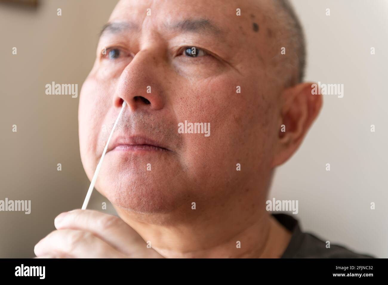 A matured Asian man taking a swab sample carrying out a Covid-19 self home test. Stock Photo