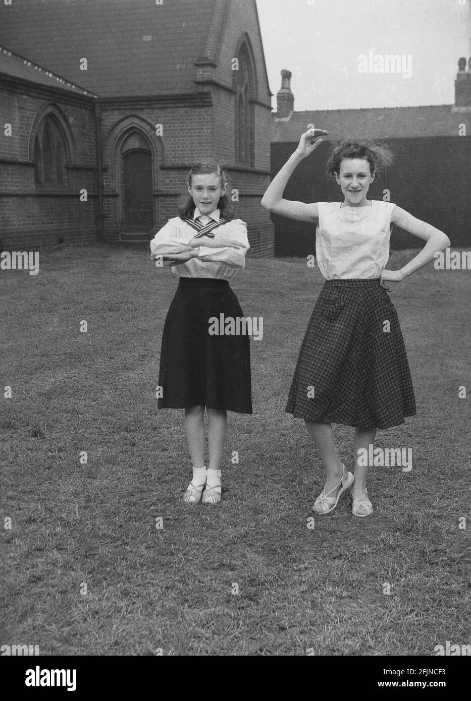 1956, historical, outside in the grounds of church, two teenage girls showing off dance moves they will perform in the May Day carnival, Leds, England, UK. An ancient festival celebrating the arrival of Spring, May Day involved the crowning of a May Queen and dancing around a Maypole, activities that have taken place in England for centuries. Selected from the girls of the area, The May Queen would start the procession of floats and dancing. In the industrialised North of England, the Church Sunday Schools often led the organisation of the carnival. Stock Photo