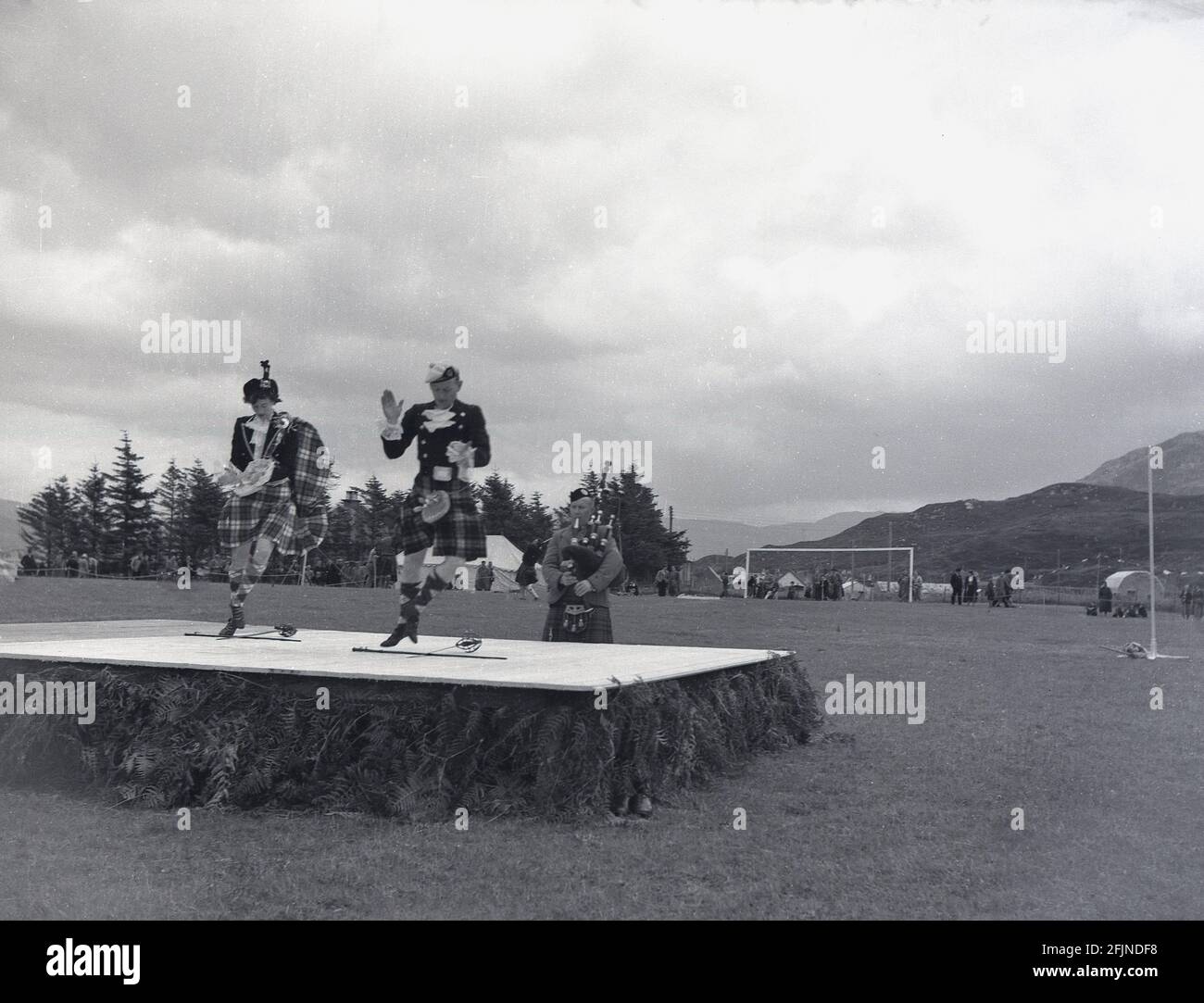1956, a male and female doing traditional scottish dancing on a wooden platform or stage in a field at a highland games at Greenock, Scotland, UK. First documented in the 1820's at Invergarry, the games would see locals demonstrate their strength and agility in various activites such as tossing the hammer. They also included scottish  ddancing and piping. The visit of Queen Victoria at the Braemer Gathering in 1848 began the Royal Association and saw them increase in popularity. Various events known as Highland Games or simply Gatherings are now held throughout Scotland in the summer months. Stock Photo