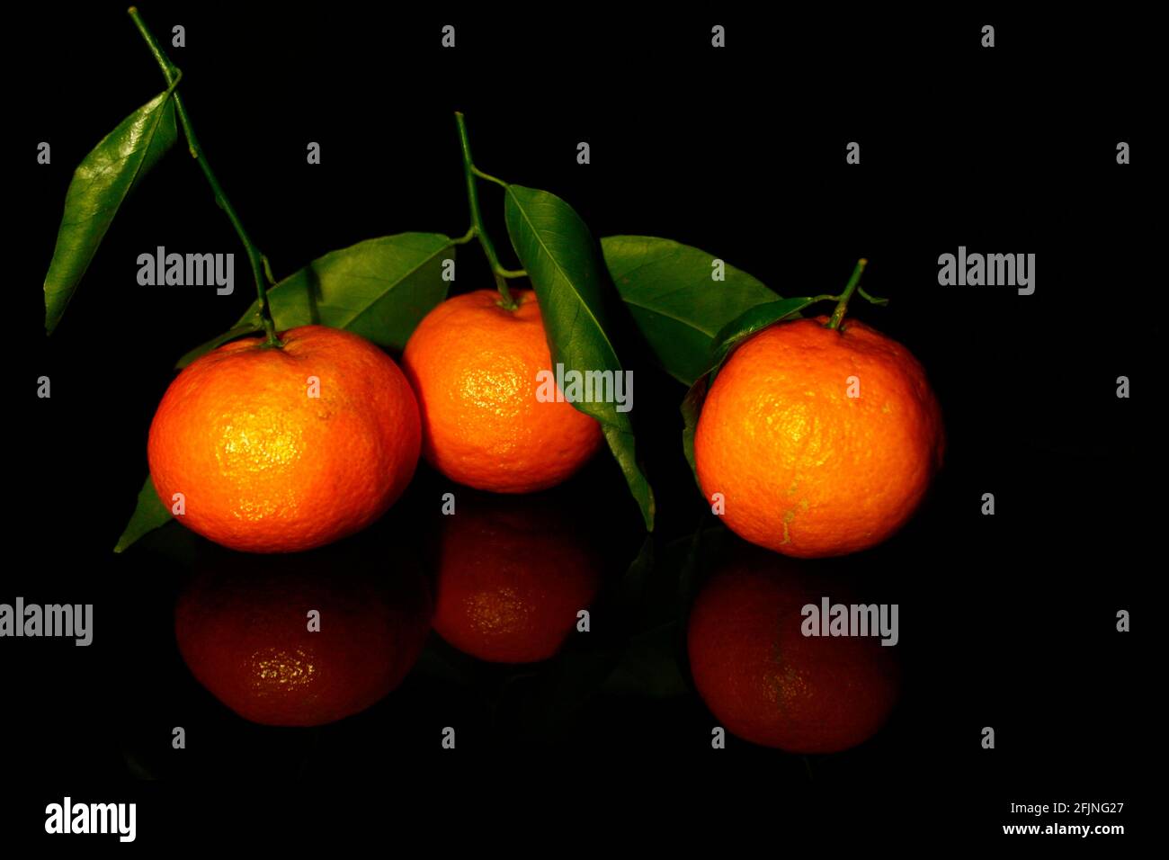 three mandarins with leaves isolated on black with reflection Stock