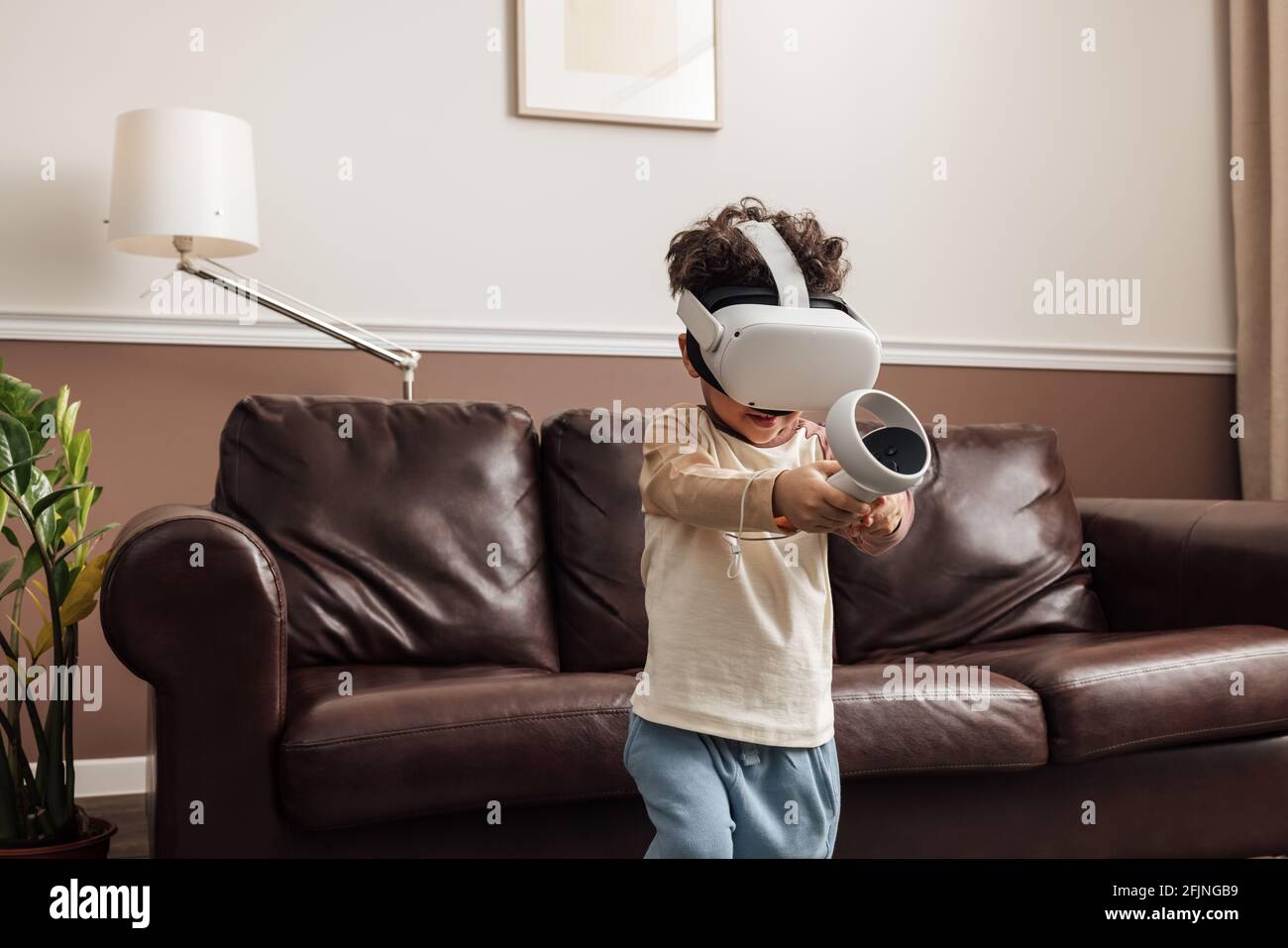 Boy wearing virtual reality headset using controller while exploring cyberspace in living room Stock Photo