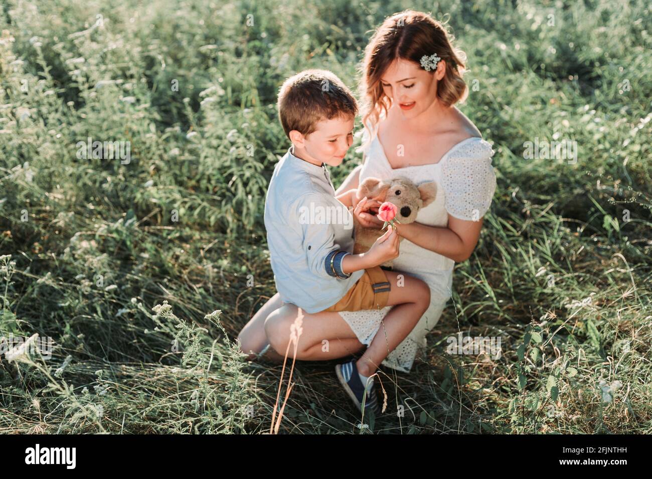 Beautiful young mom holding her blond son in her arms while he is holding a rose. Outdoor photo. Mothers day Stock Photo