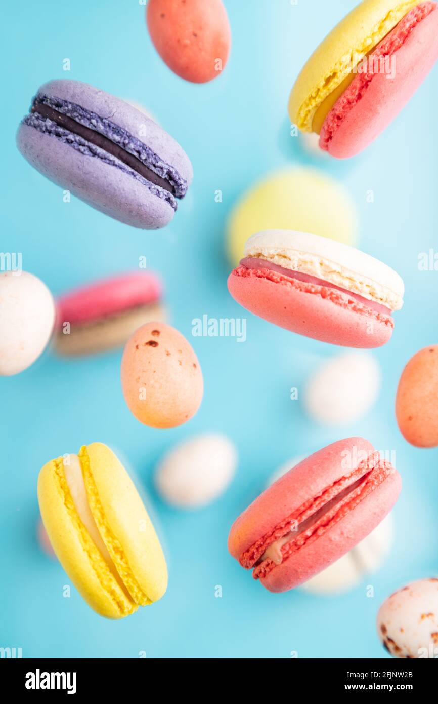 Multicolored flying macaroons and chocolate eggs frozen in the air on blurred blue background. top view, flat lay, close up. Breakfast, morning, conce Stock Photo