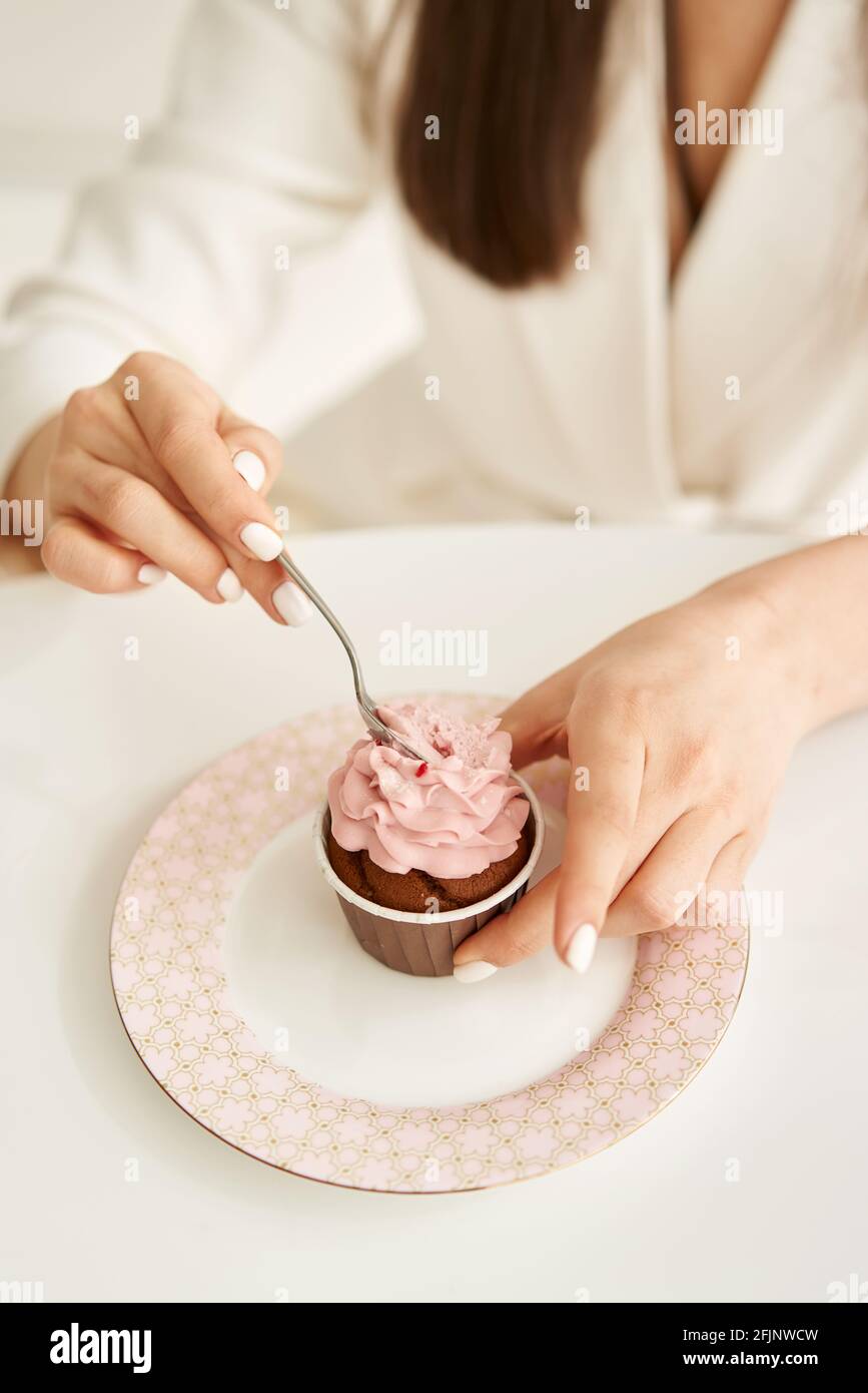 woman eating pink cupcake on the plate, by little spoon Stock Photo