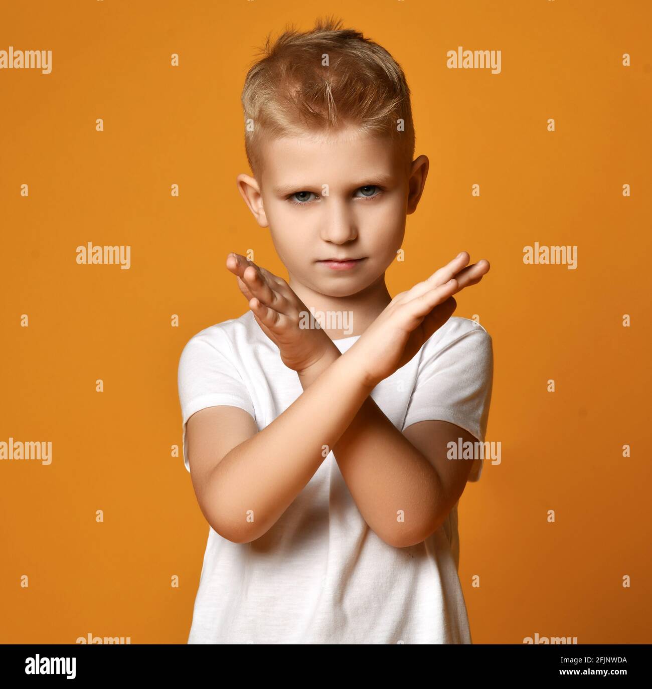 Blond boy child in white t-shirt and jeans standing and showing stop rejection sign by hands looking at camera Stock Photo