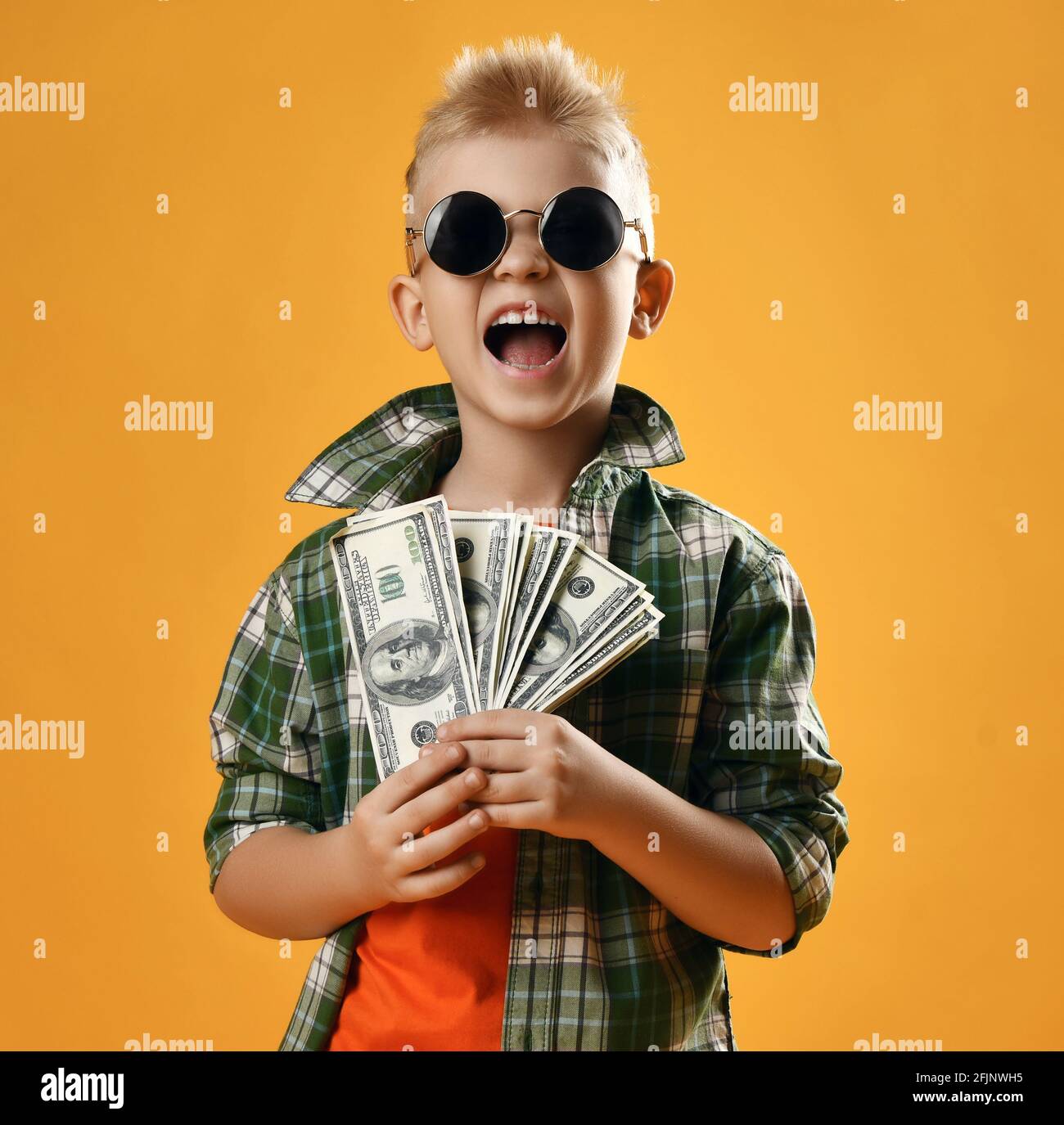 Blond smiling boy child in checkered shirt and sunglasses standing holding heap of money cash in hands feeling happy Stock Photo