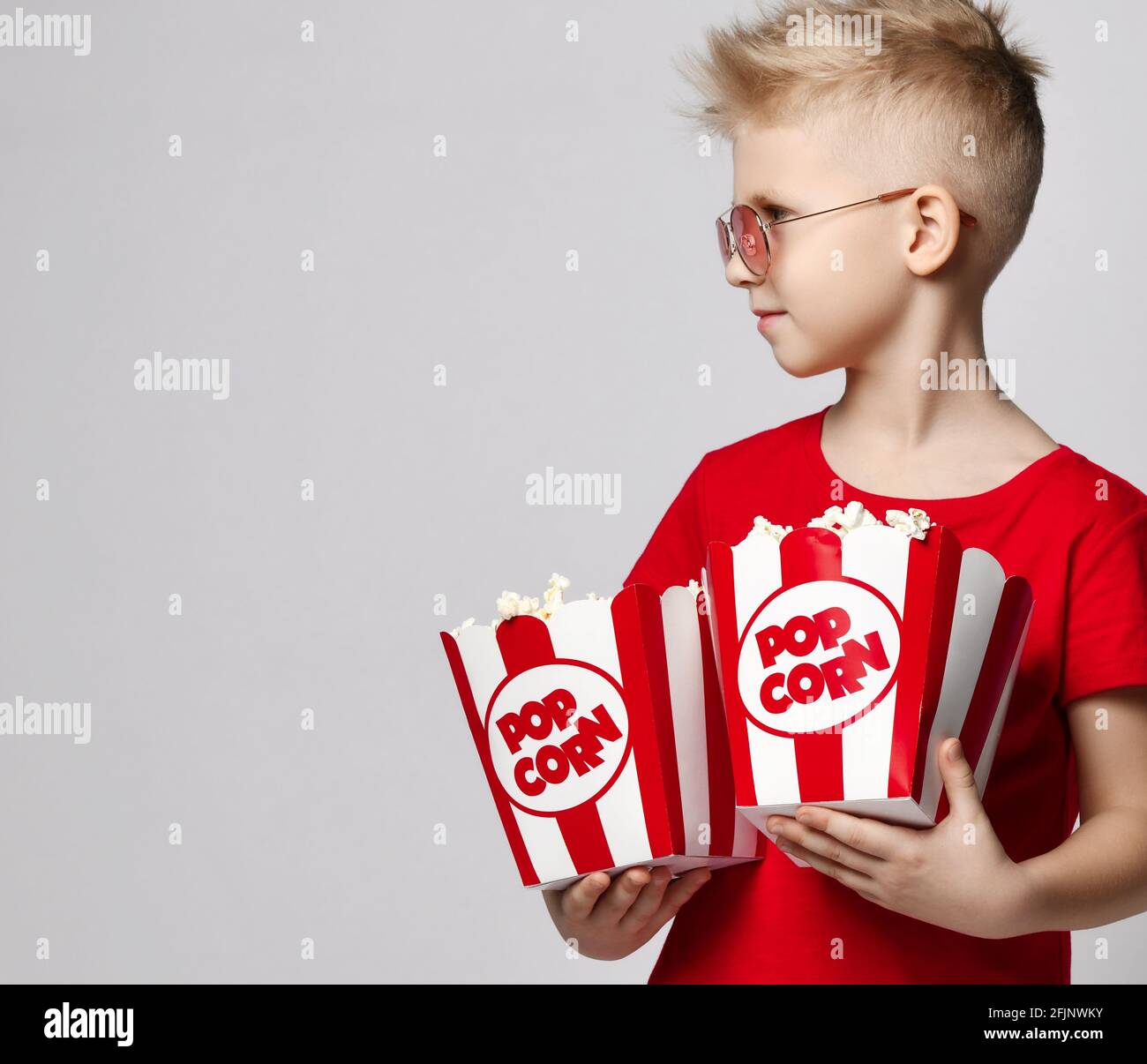 Stylish cheerful boy child in red t-shirt holding pop corn in hands looking away over white background. Trendy casual children Stock Photo