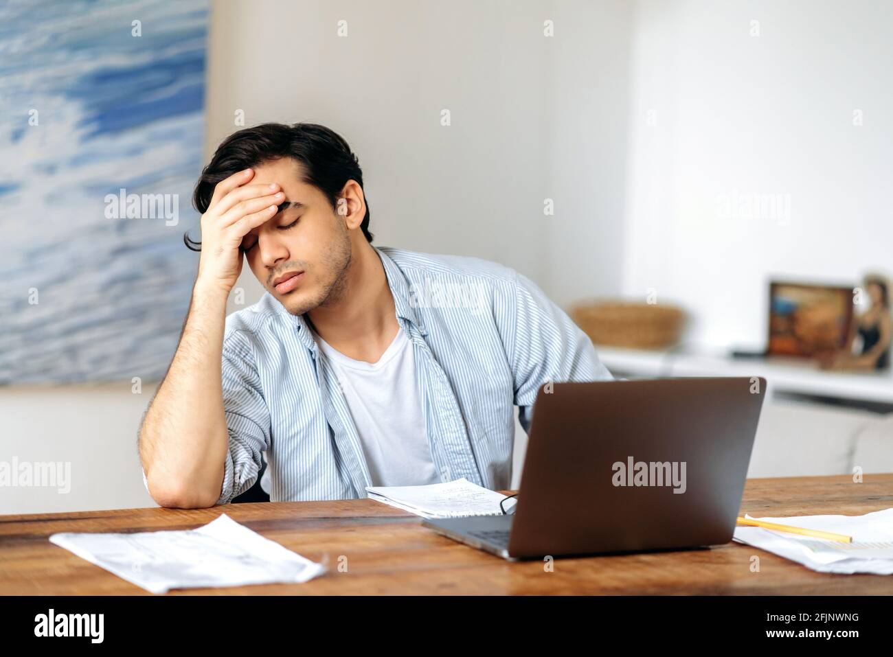 Tired jaded mixed race hispanic guy, employee, freelancer or student, in casual clothes, working or studying at laptop, experiencing stress at work, headache, need a rest, eyes closed Stock Photo