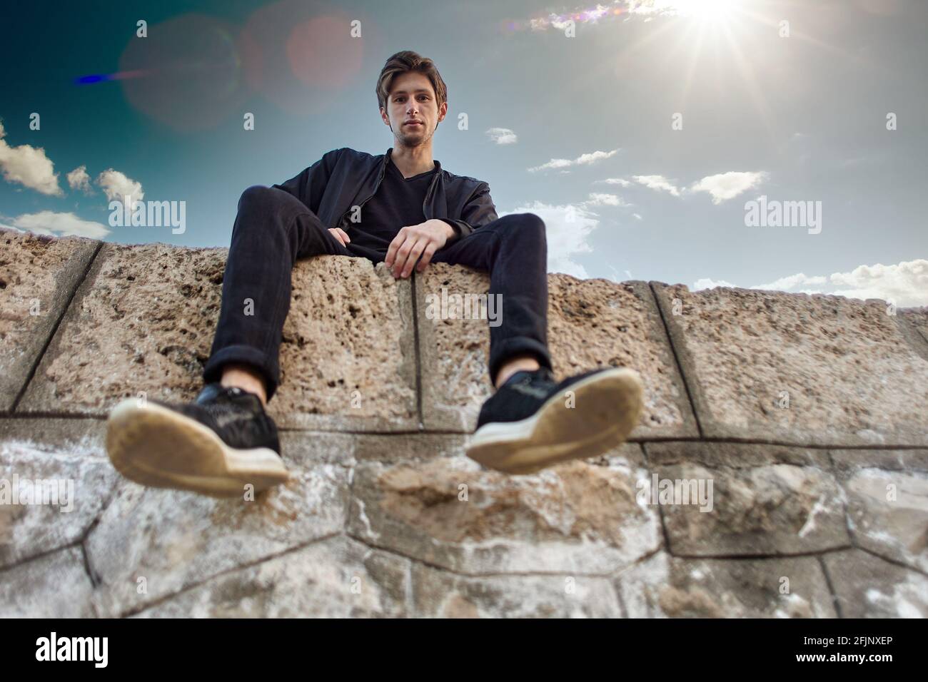 Bottom view of young Caucasian male sitting on stones of pier. Stock Photo