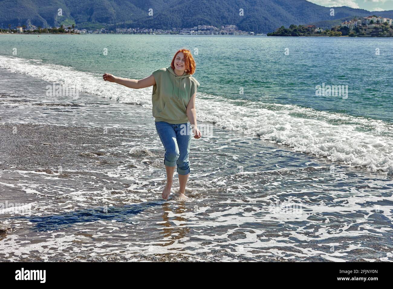 Young woman walks barefoot on beach in surf zone. Stock Photo