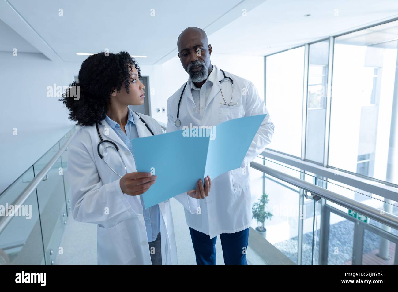 Diverse male and female doctor talking seriously and reading patient file in hospital corridor Stock Photo