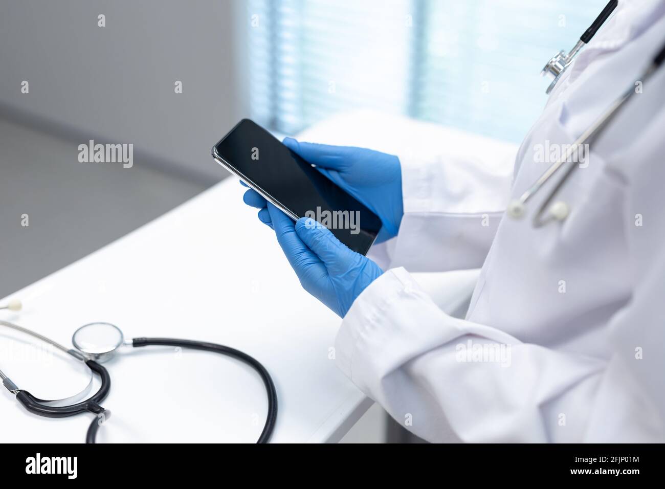 Midsection of doctor wearing latex gloves using smartphone with copy space on screen Stock Photo