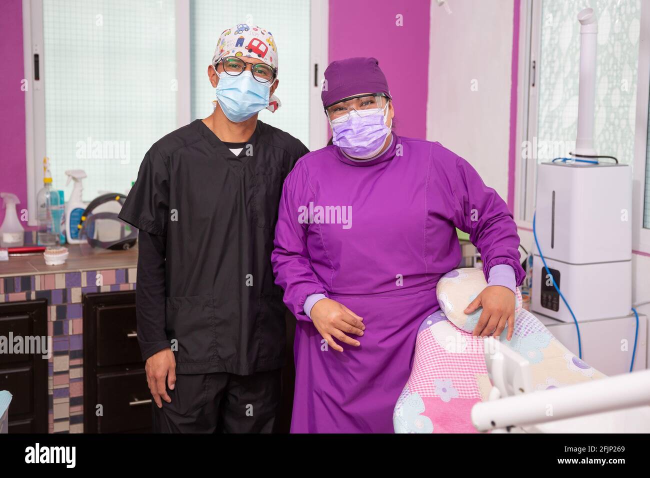 A Mexican female dentist in a purple outfit wearing a mask and goggles