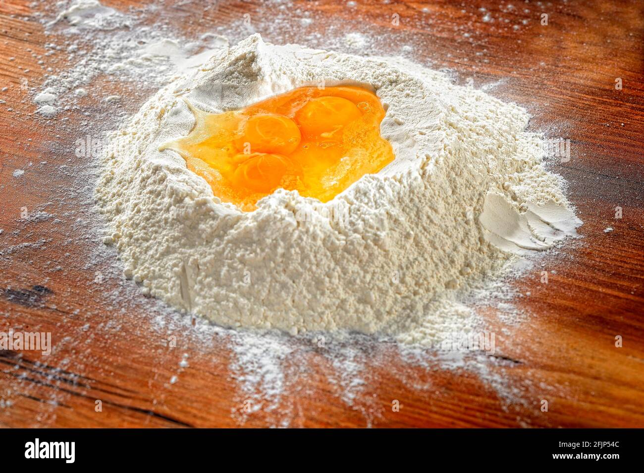 Flour with eggs on wooden table, Germany Stock Photo