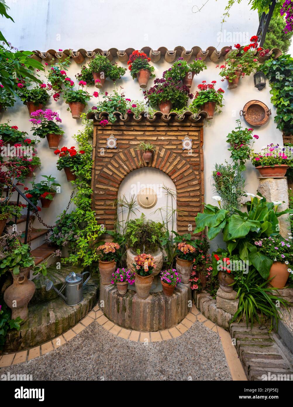 Fountain in the courtyard decorated with flowers, geraniums in flower pots on the house wall, Fiesta de los Patios, Cordoba, Andalusia, Spain Stock Photo