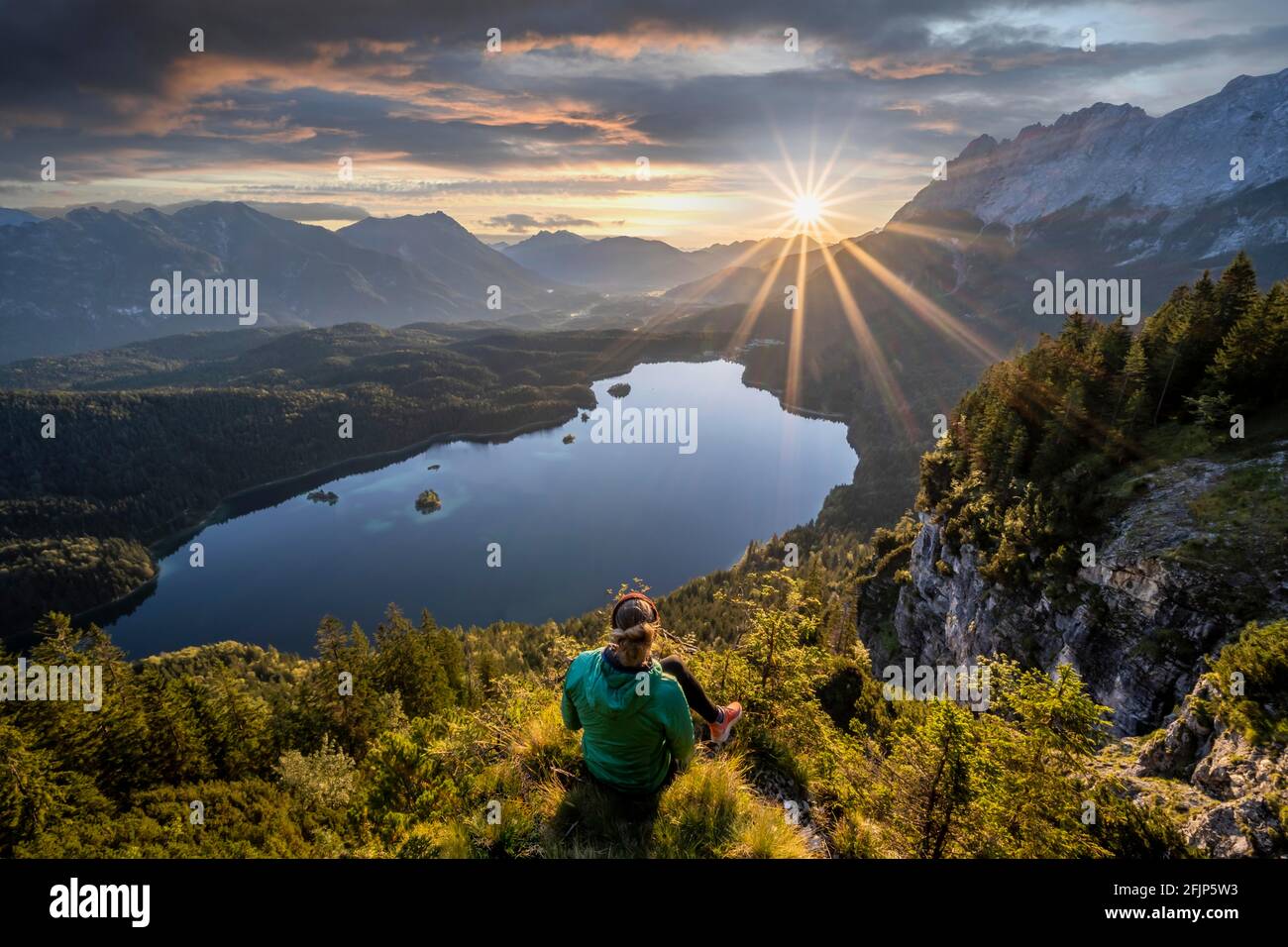 Hiker looking at Eibsee lake at sunrise, sun shining over Bavarian alpine foothills, right Zugspitze, Wetterstein mountains near Grainau, Upper Stock Photo
