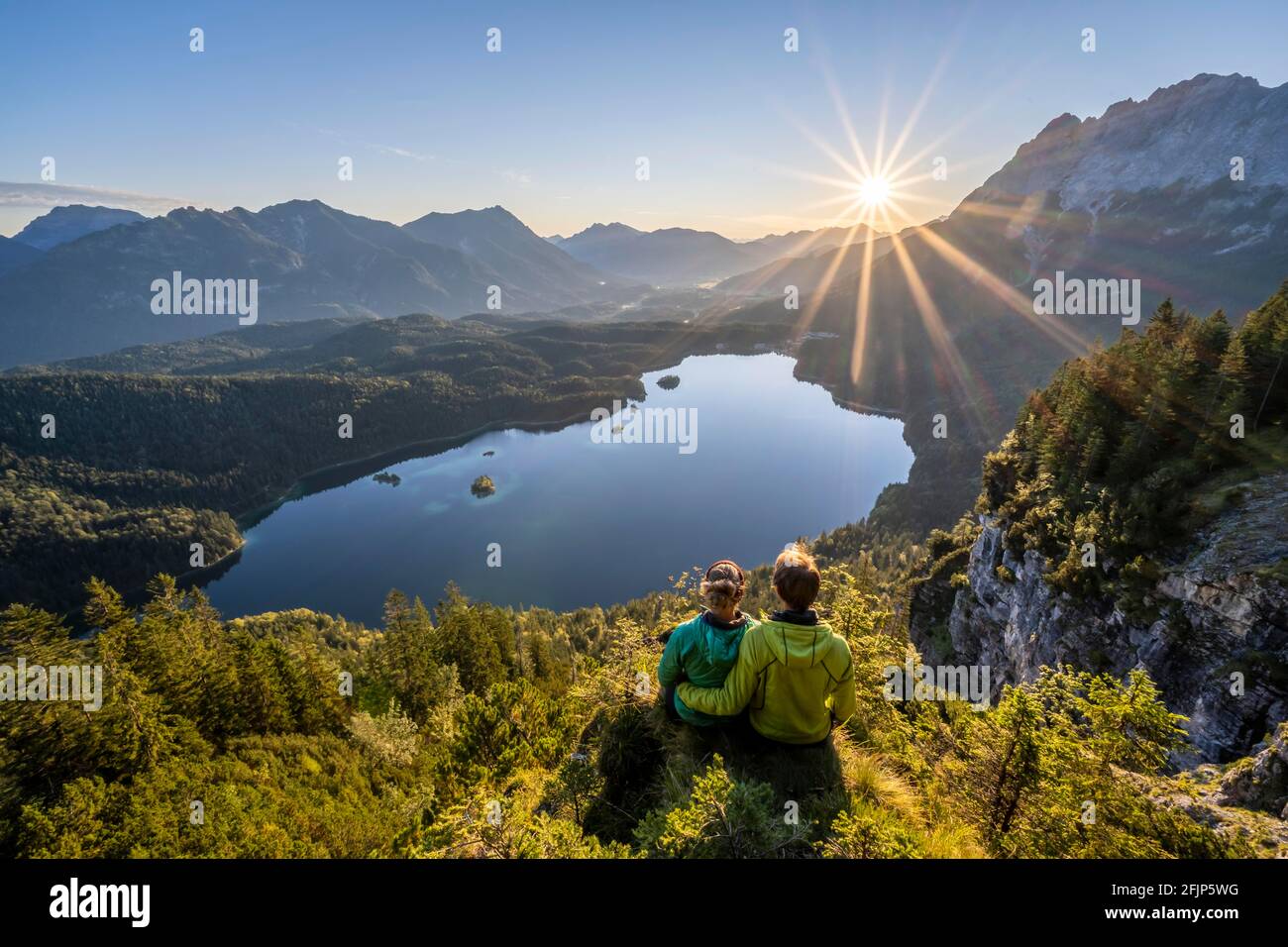 Two (hikers) looking at Eibsee lake at sunrise, sun shining over Bavarian alpine foothills, right Zugspitze, Wetterstein mountains near Grainau Stock Photo