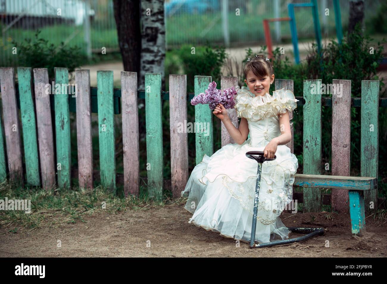 Little girl with a bouquet of lilacs sitting on a bench in the street ...