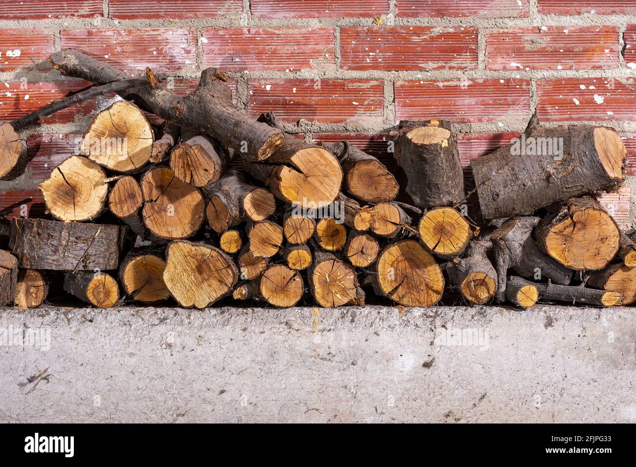 Firewood stacked on concrete and a brick wall.The photograph is a horizontal shot. Stock Photo