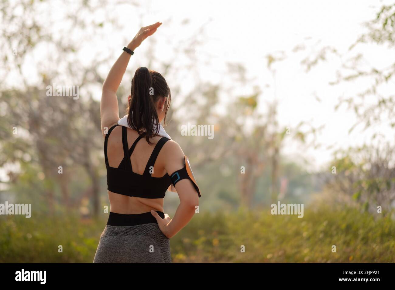 Athletic woman warming up before a workout standing facing the early morning rising sun at park Stock Photo
