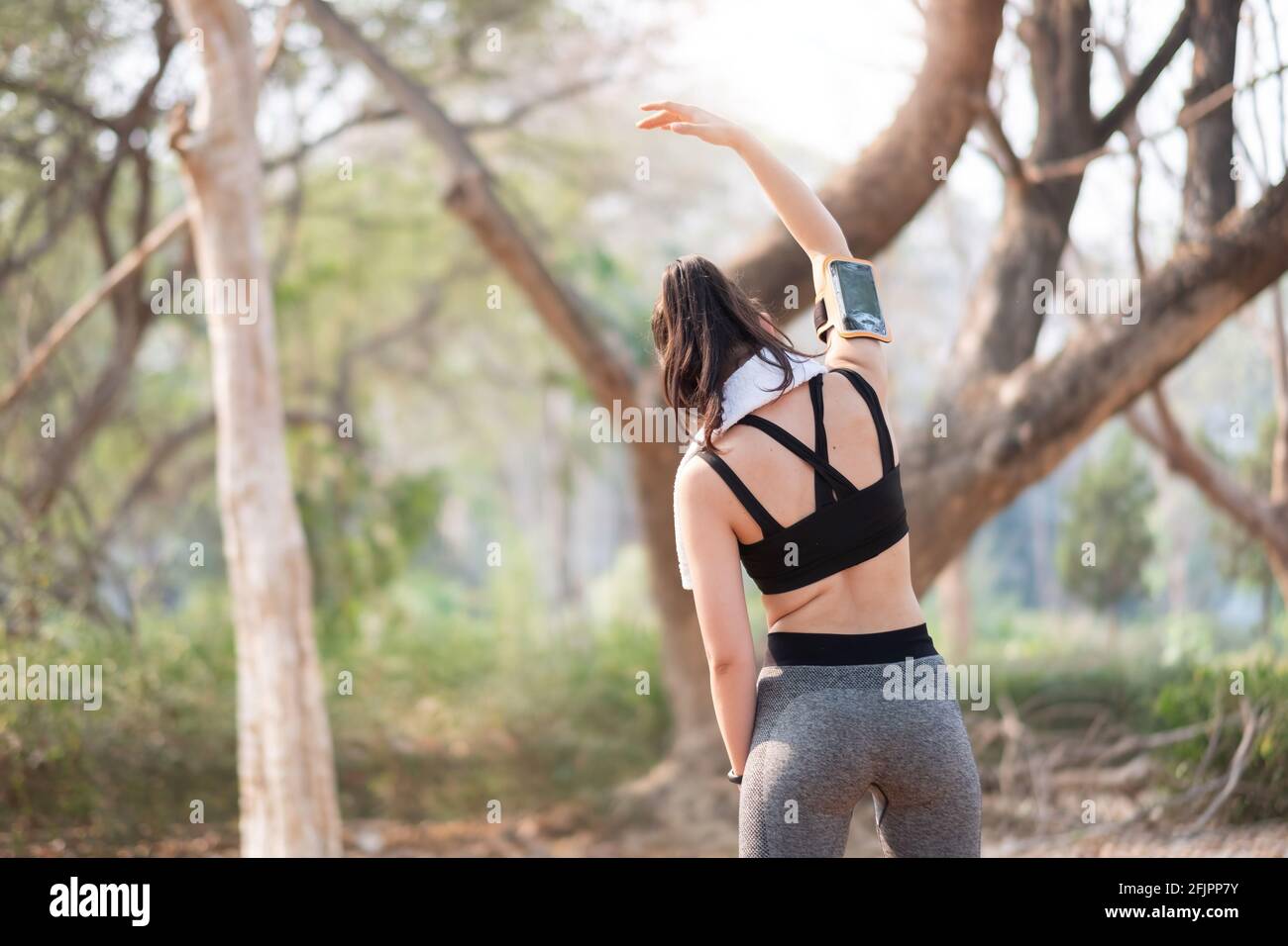 Athletic woman warming up before a workout standing facing the early morning rising sun at park Stock Photo