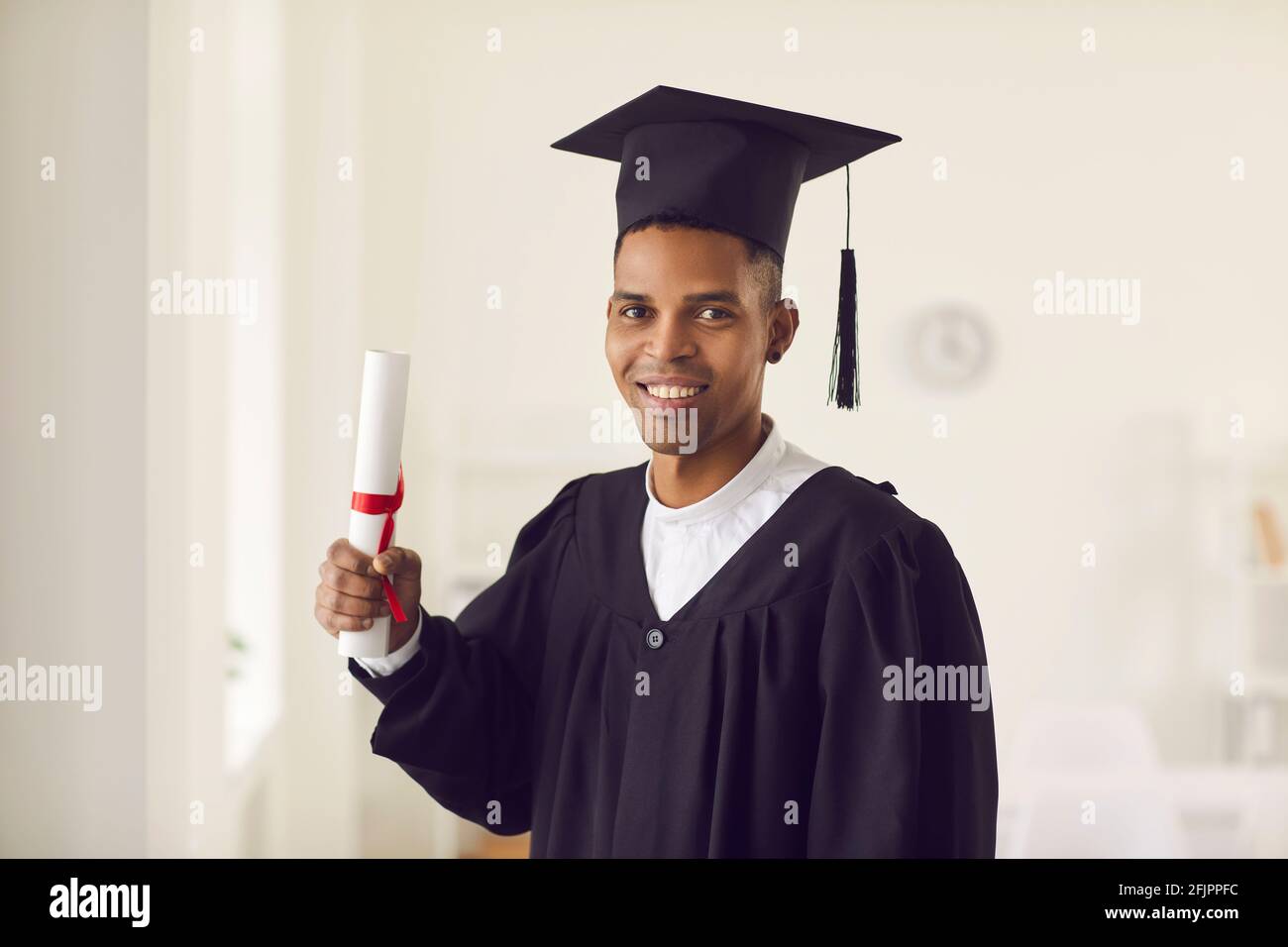 African-American student in black academic gown and cap holding diploma and smiling Stock Photo