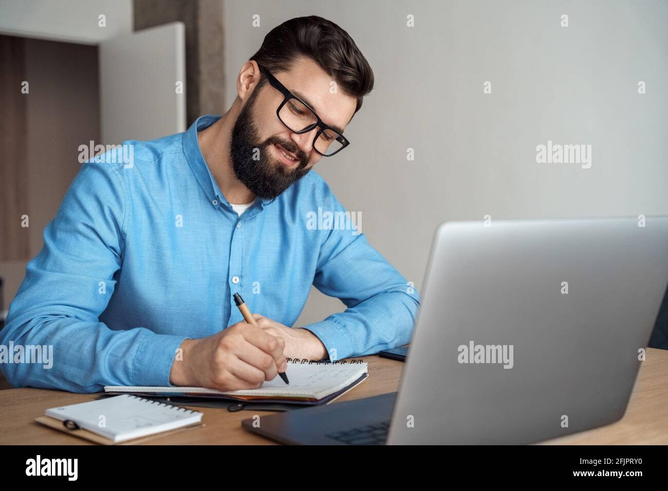 Millennial male student making notes watching webinar on laptop computer Stock Photo