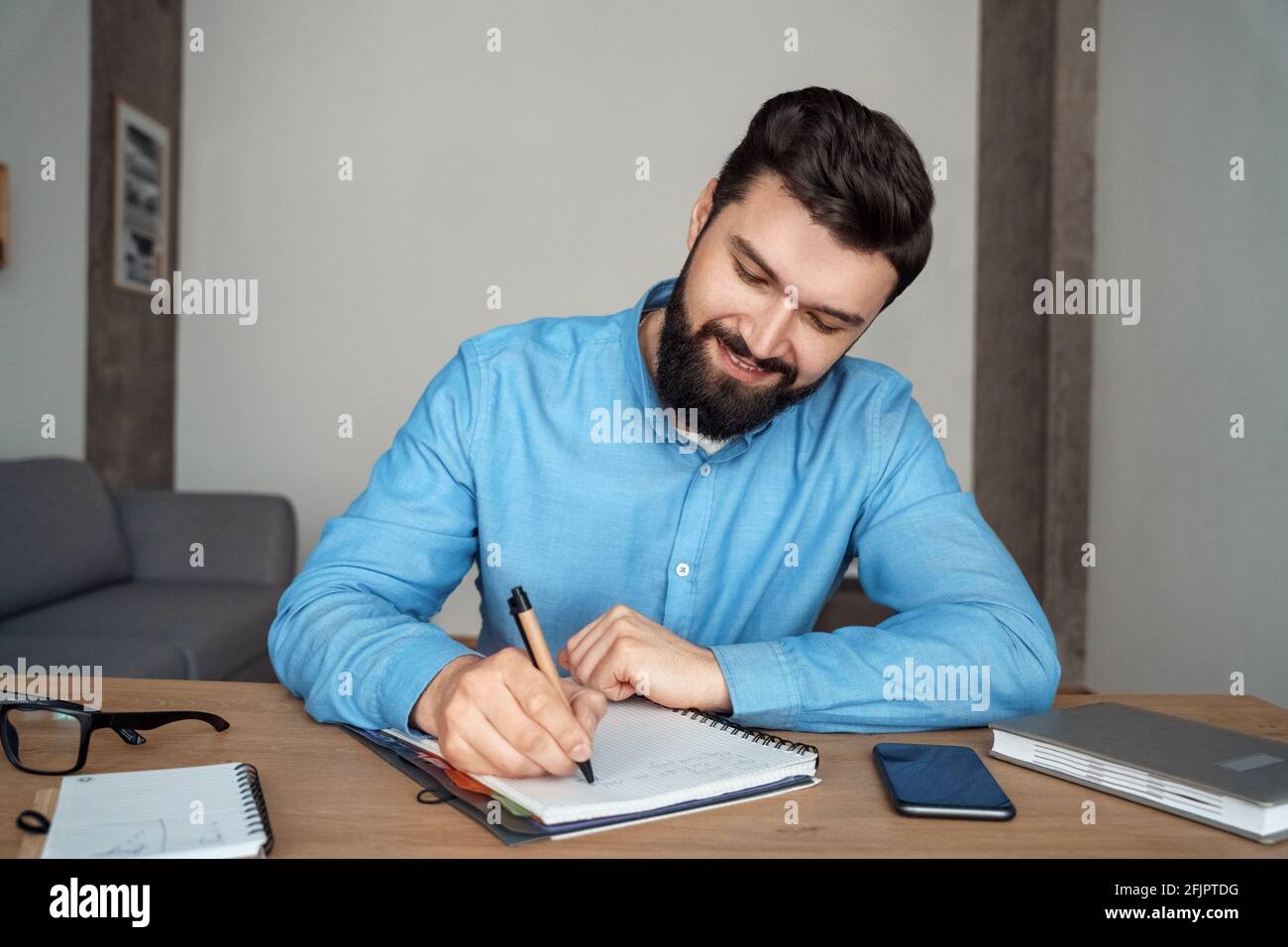 Smiling man student sitting at desk writing in notebook on online webinar lesson Stock Photo