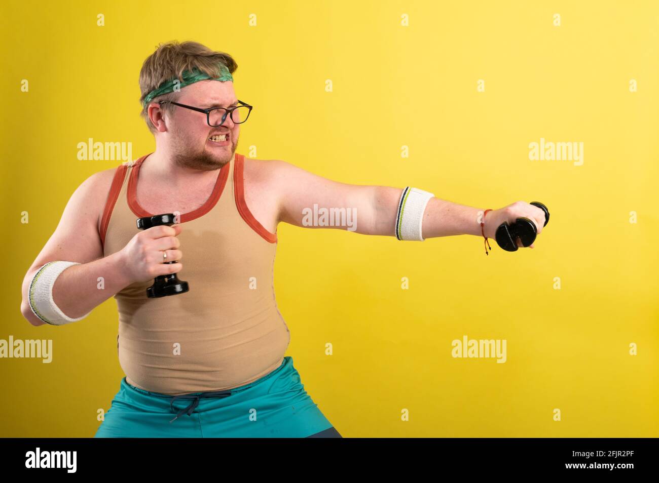 fat man wearing black shirt exercising with dumbbells and looking at camera Stock Photo