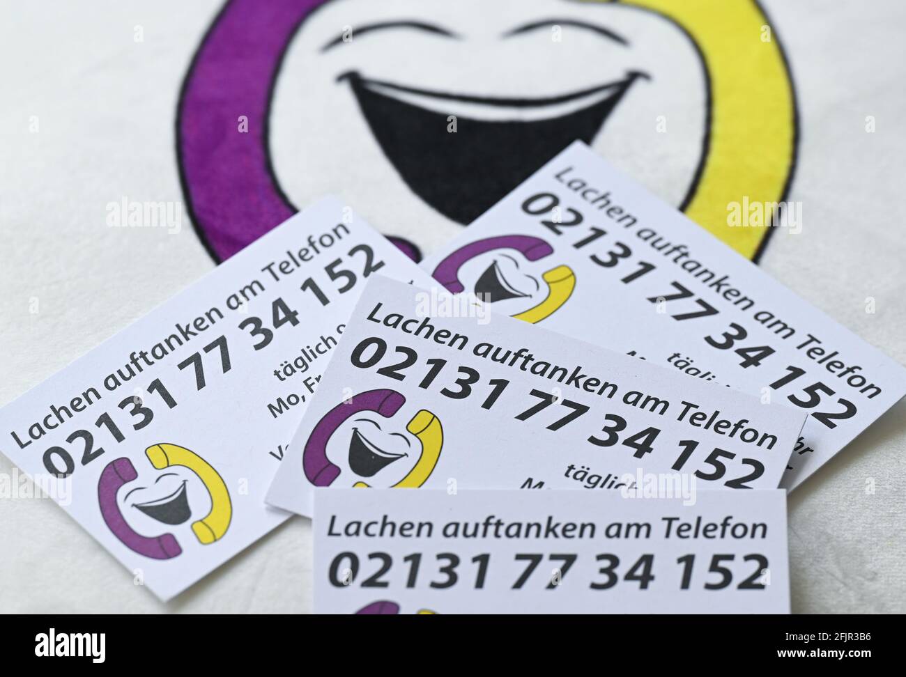 22 April 2021, Hessen, Hanau: ILLUSTRATION - Business cards with the inscription 'Lachen auftanken am Telefon' and the telephone number 02131 77 34 152' lie on a cushion with the logo of the 'Lachlefon' in the practice of Sandra Mandl, alternative practitioner for psychotherapy and laughter yoga teacher. The Hanauer therapist belongs to the approximately 40-strong team of the 'Lachlefon', which was founded about a year ago. It addresses itself to all, which need a fast tendency brightening. Under the daily twelve hours attainable laughter telephone number all age groups call from children to h Stock Photo