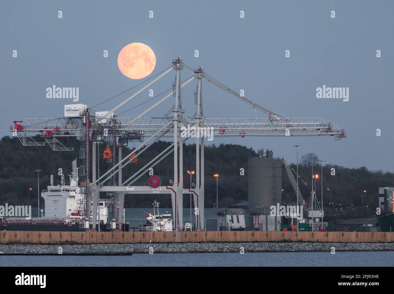 Ringaskiddy, Cork, Ireland. 26th April, 2021. A super full Pink Moon descends behind the gantry cranes and bulk carrier Pilatus Venture at the new Port of Cork deep water terminal at Ringaskiddy, Co. Cork, Ireland. - Credit; David Creedon / Alamy Live News Stock Photo