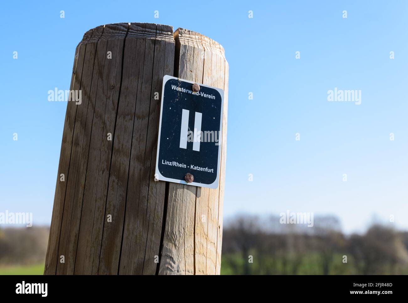 Wooden pole with waypoint or direction sign, Westerwald-Verein, Linz Rhein, Katzenfurt, along a hiking path against blue sky in Germany, Europe Stock Photo