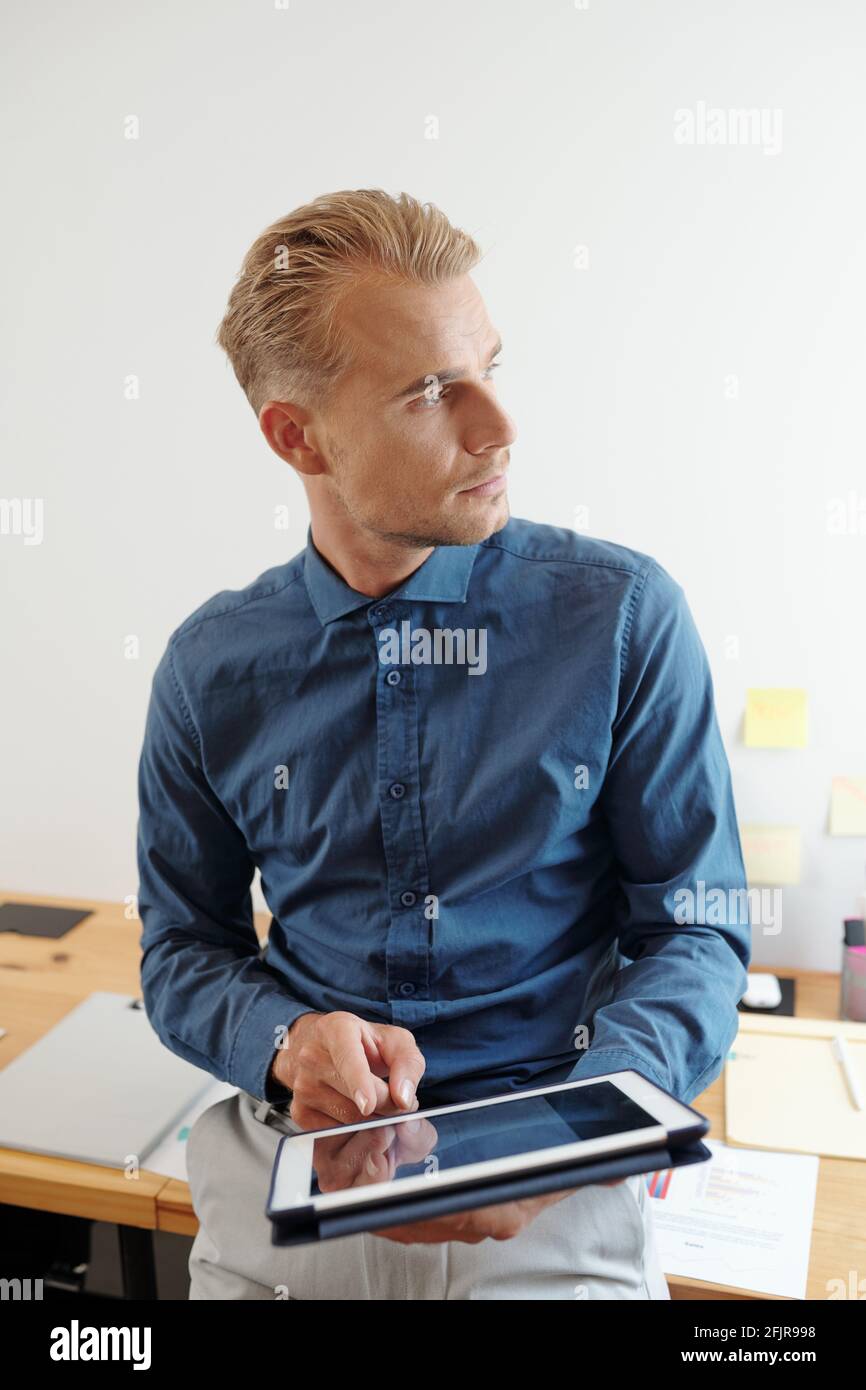 Portrait of young handsome entrepreneur using application on tablet computer and looking through office window Stock Photo